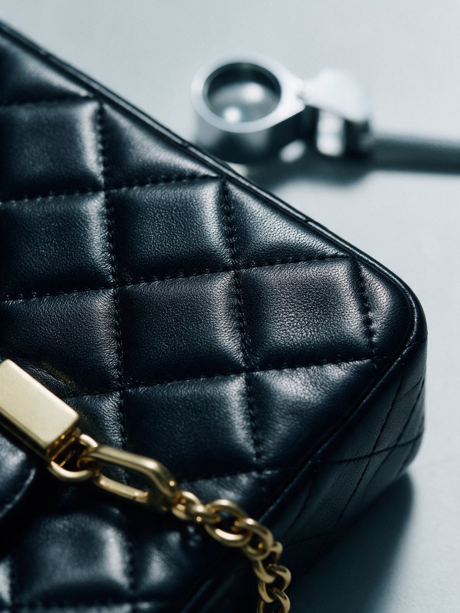 Extreme close-up of quilted leather stitching and a gold chain link with a jeweller's loupe behind