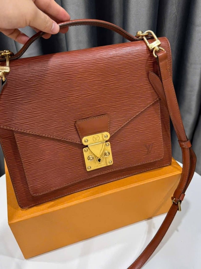 Cognac leather top-handle flap bag with a gold S-lock, shown on its box